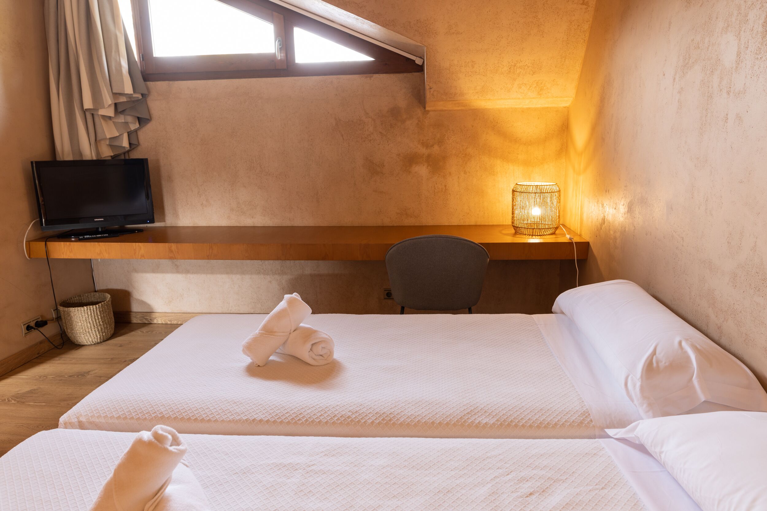 A hotel room with a bed, a desk, a chair, a TV, and a lamp.