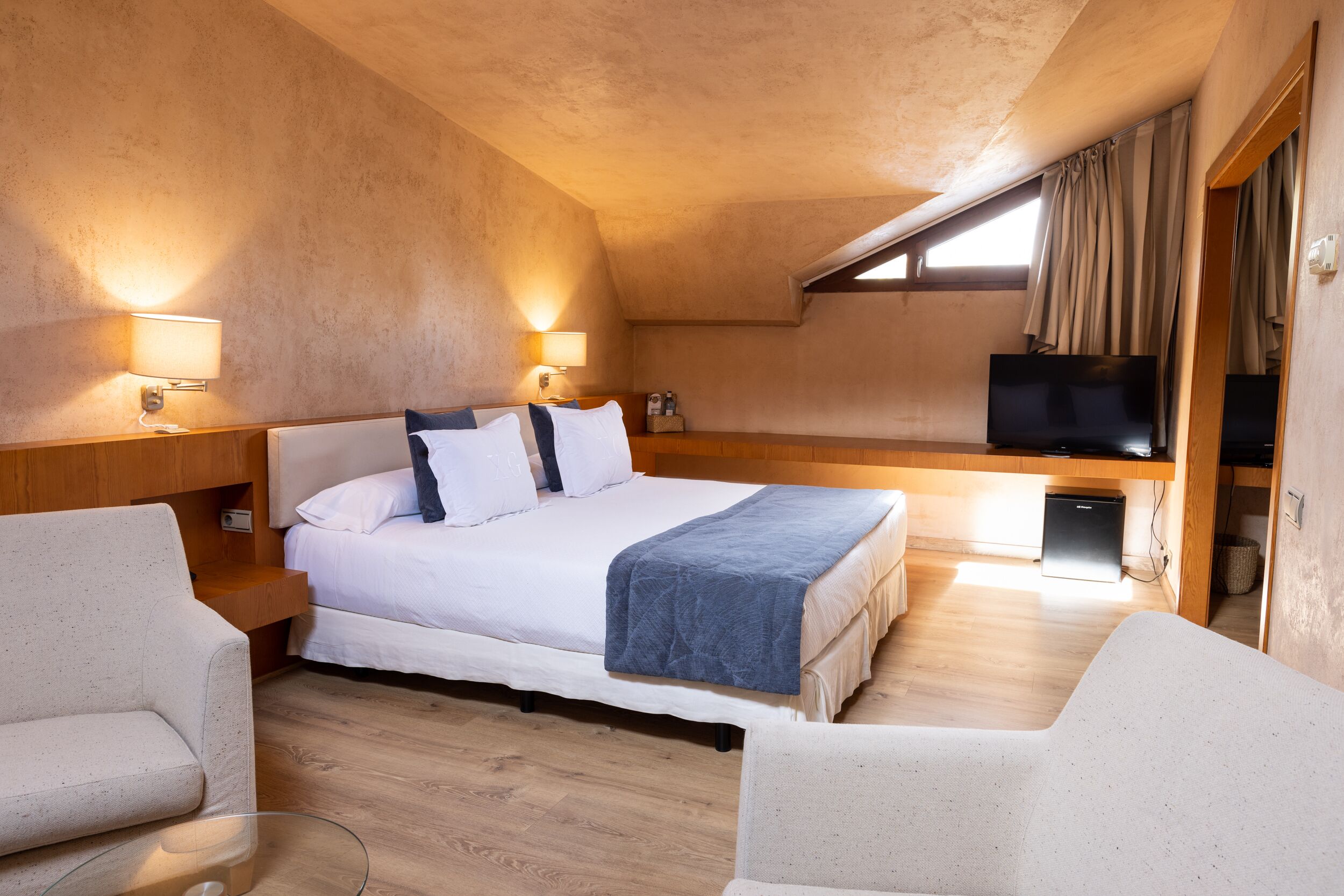 A bedroom with a bed, bedside lamps, a TV, and a small desk.