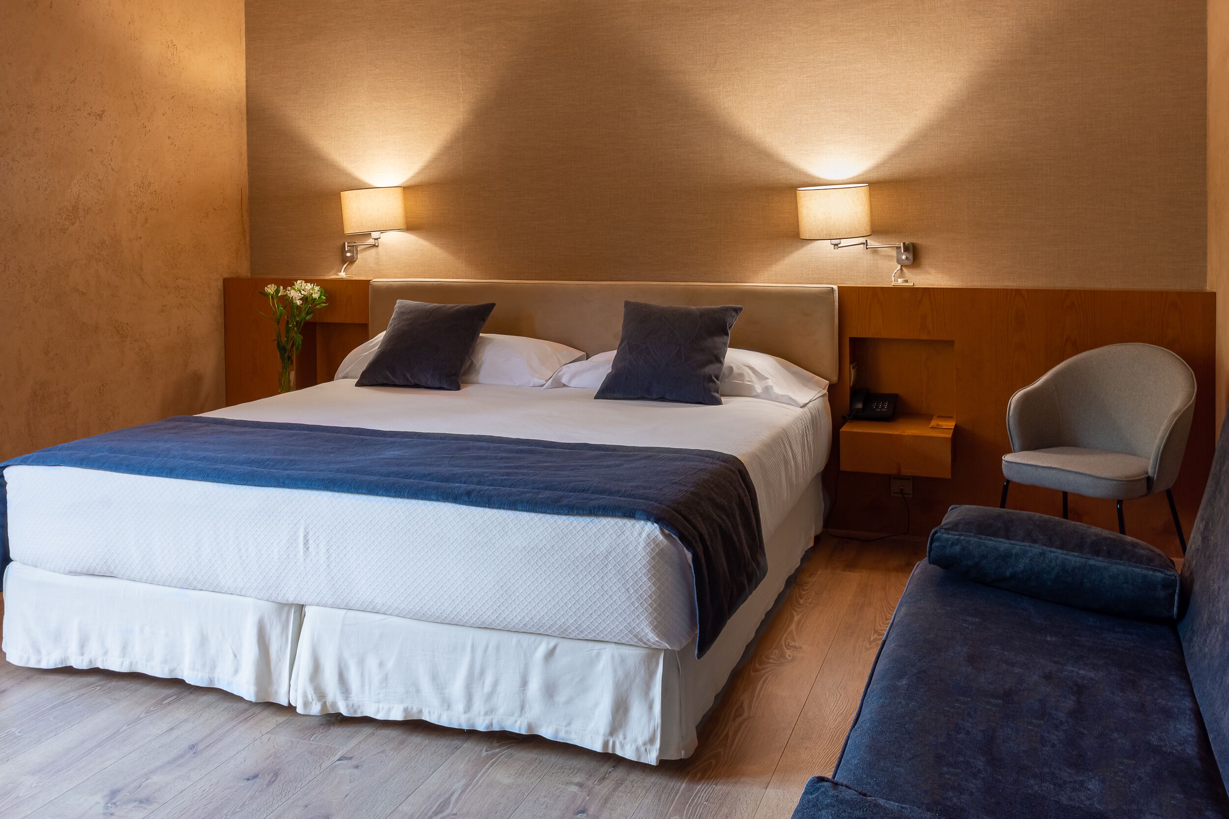 A hotel room with a large bed, two bedside lamps, a chair, and a bedside table.