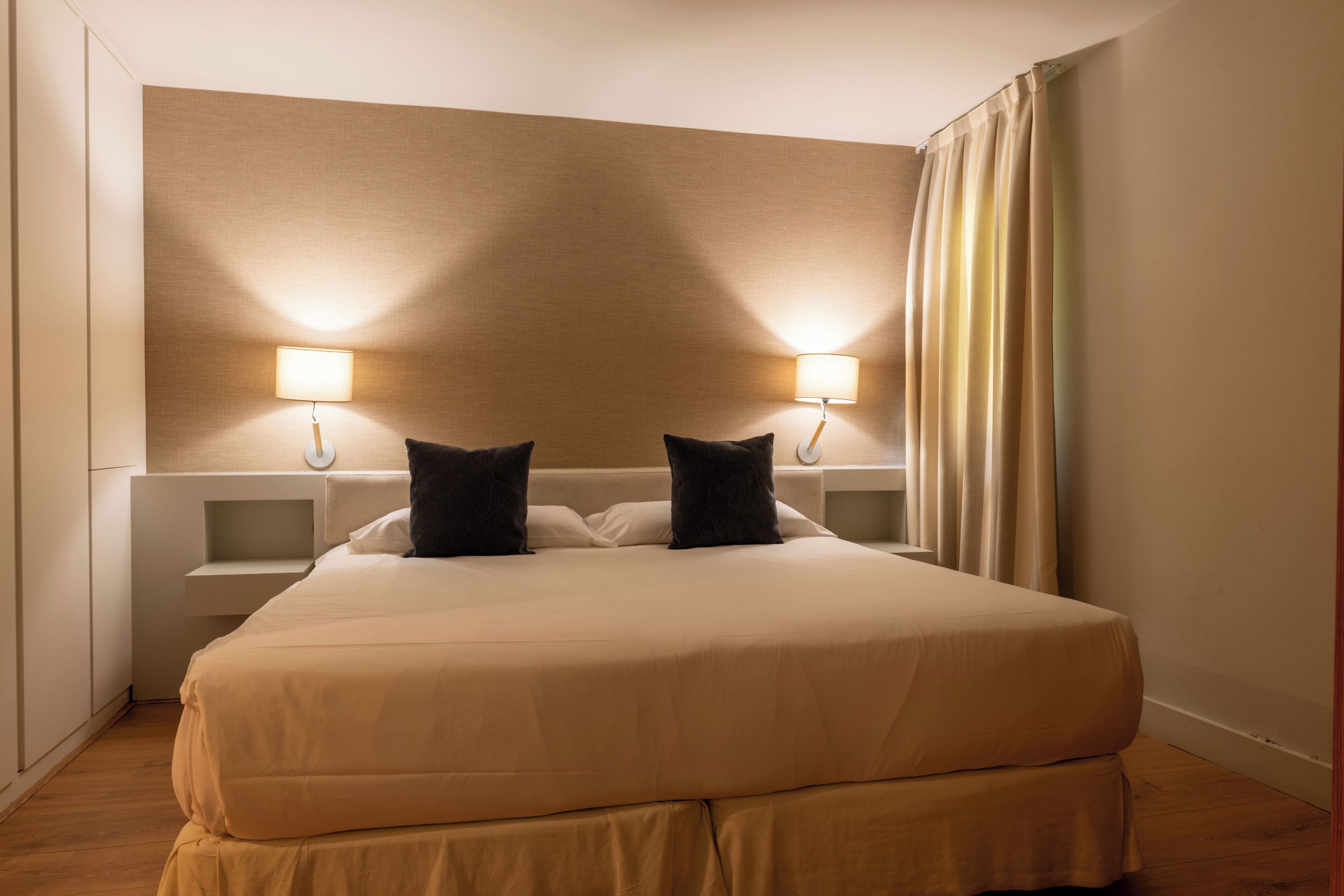 Ein Hotelzimmer mit einem großen Bett, zwei Nachttischlampen, einem Nachttisch und einem Vorhang.