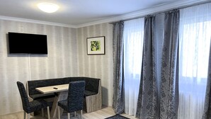 A room with a wooden dining table, two chairs, a flat-screen TV, a framed picture, and a patterned rug.
