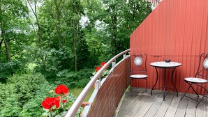 A wooden deck with metal chairs and a table, surrounded by a red wall and lush greenery.