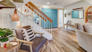Uma sala de estar moderna com escada de madeira, porta azul e planta em vaso.