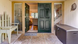 Uma entrada frontal com uma porta verde escura, um banco, um tapete com a palavra “WELCOME” e um grande aquecedor de metal.
