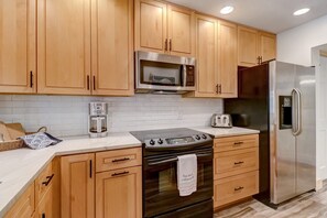 Une cuisine moderne avec des meubles en bois, un réfrigérateur en acier inoxydable, un four à micro-ondes, une cuisinière et une machine à café.