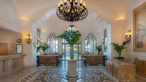 Un lobby imponente con una columna de mármol central, candelabros ornamentales y un suelo con diseño.