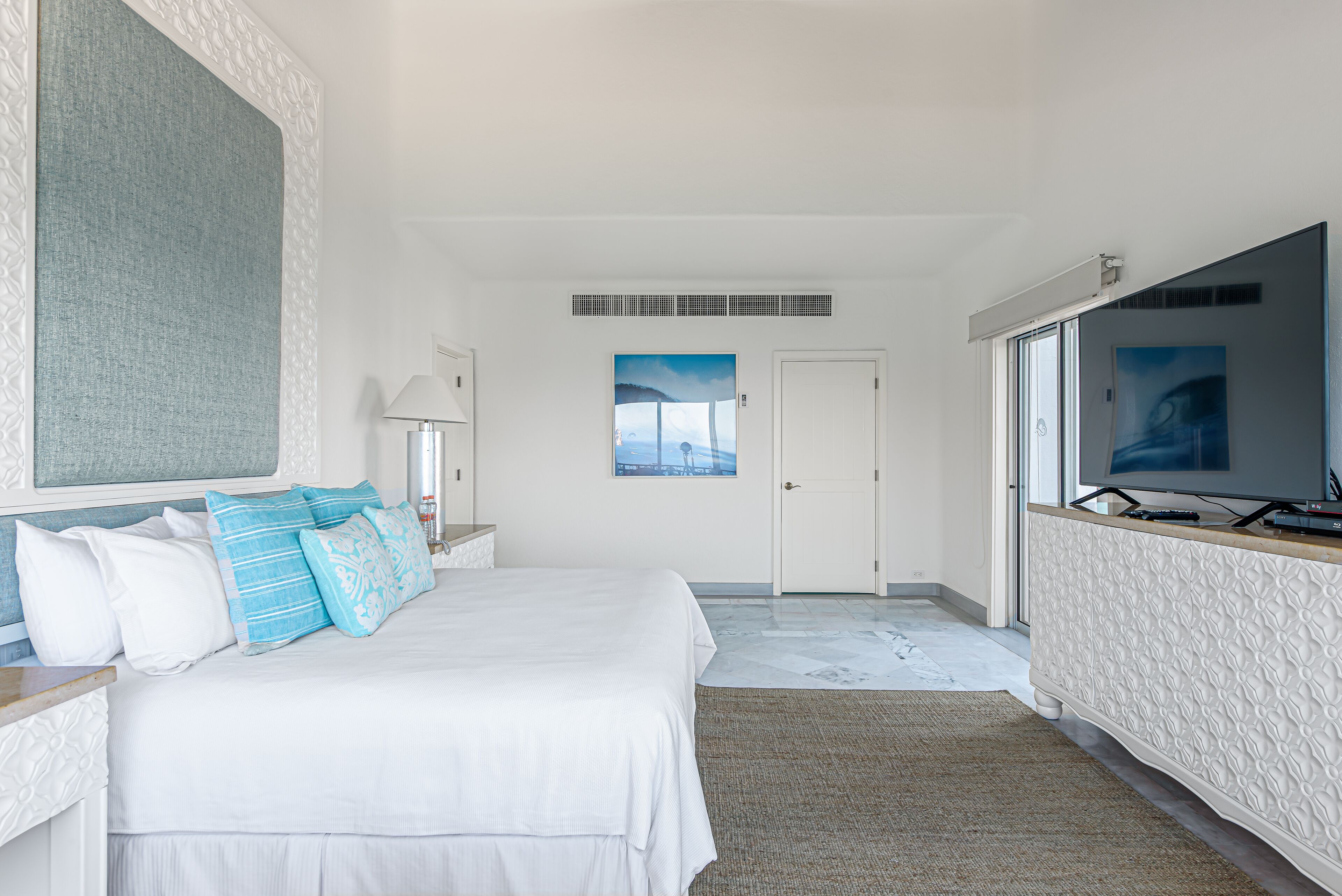 A hotel room with a large bed, a television, a window with a view, and a door.