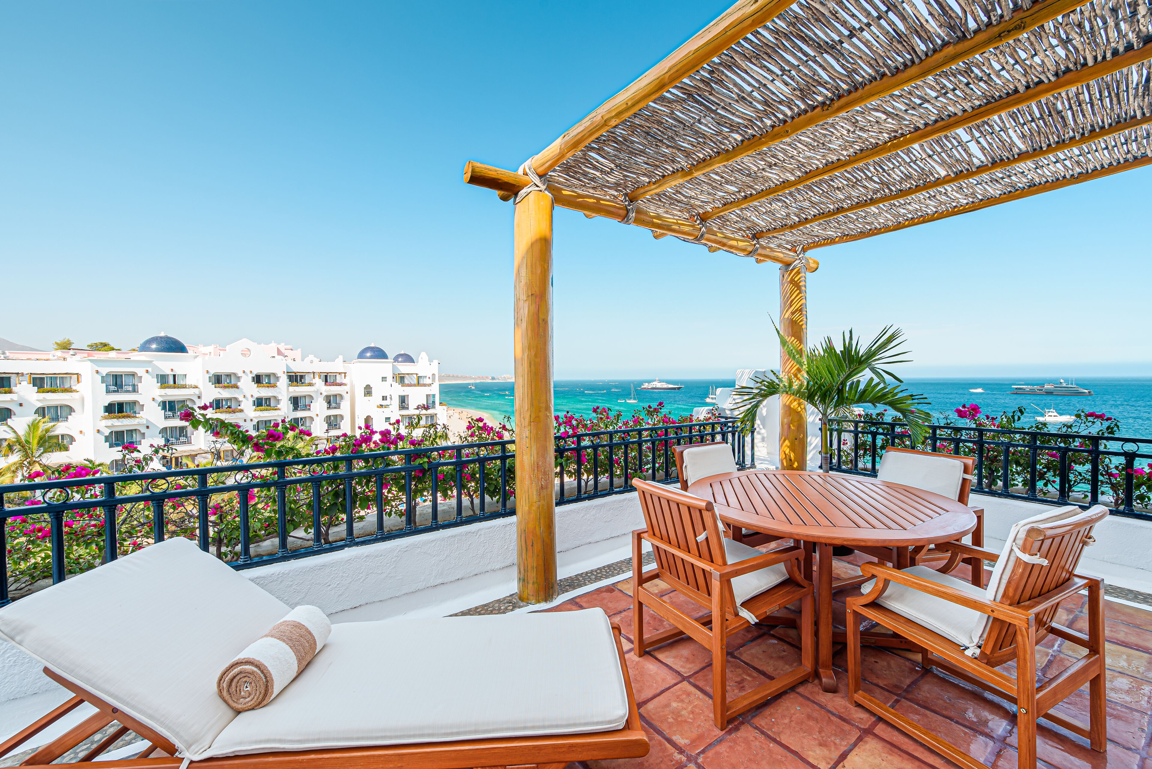 Une terrasse avec une table et des chaises en bois, un fauteuil de relaxation et une vue sur la mer et les bâtiments en arrière-plan.