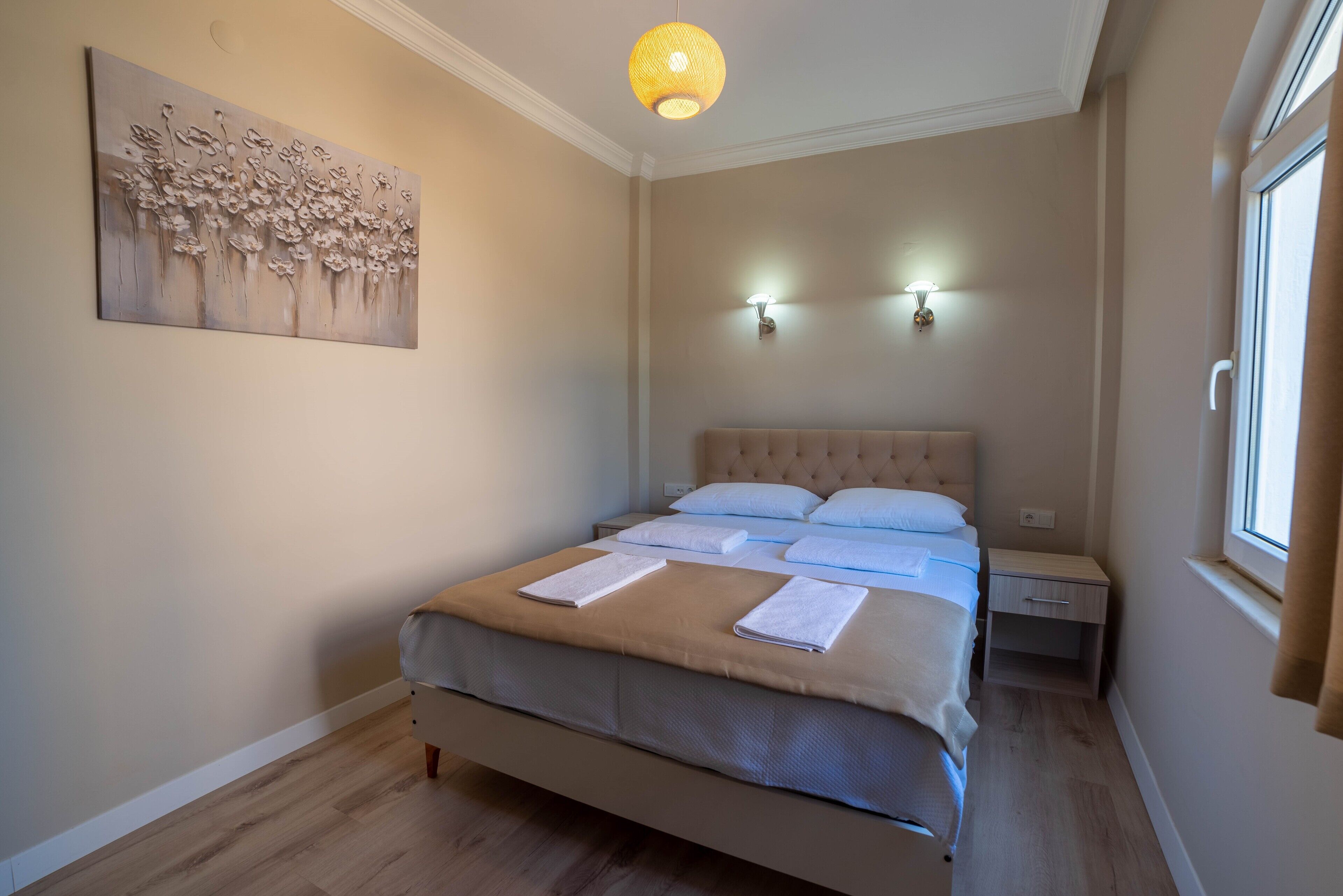 Une chambre à coucher avec un grand lit, deux tables de chevet, un luminaire fixé au mur et une fenêtre.