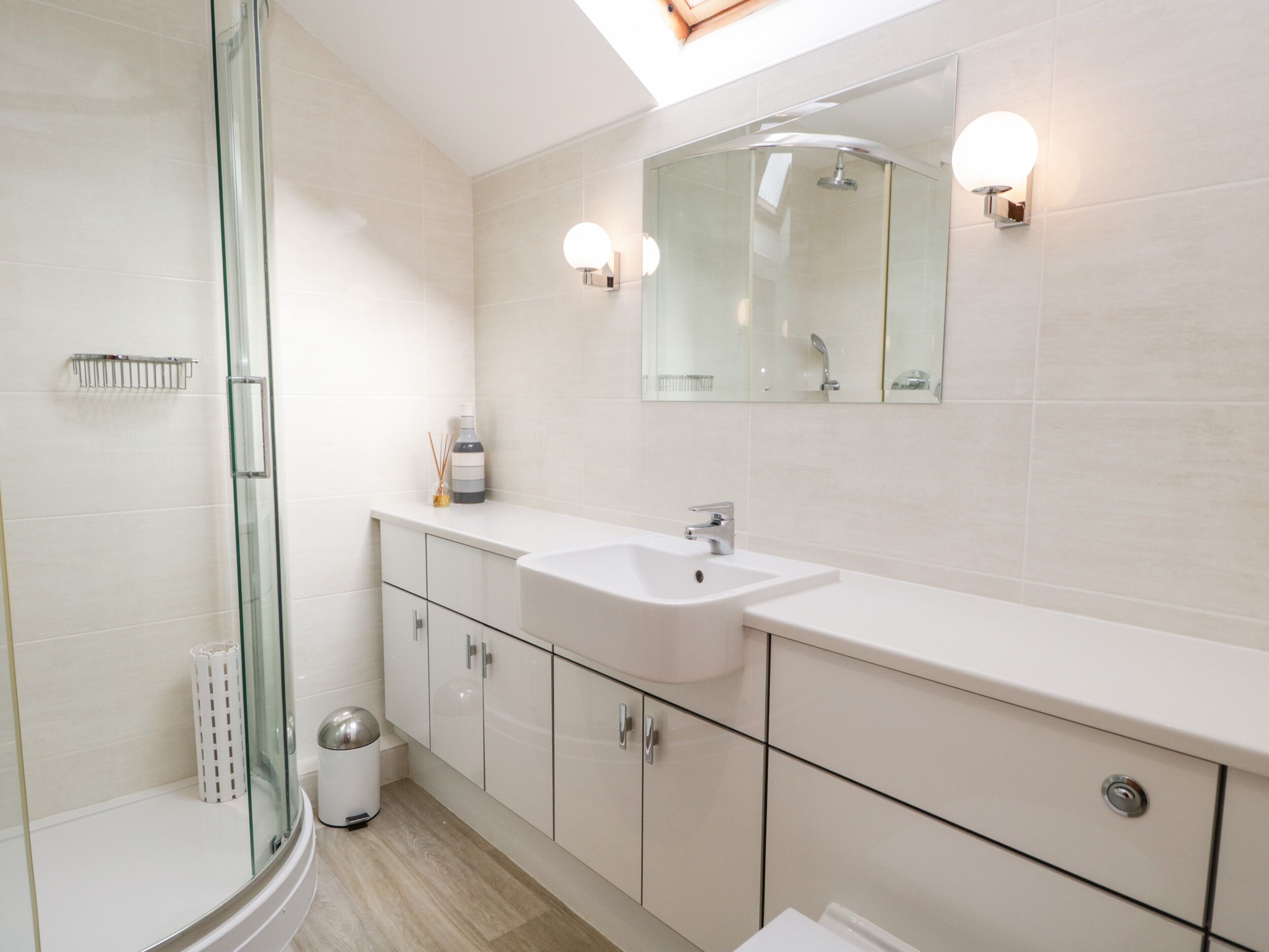 Een moderne badkamer met een glazen douchecabine, een wit wastafelmeubel en een spiegel met wandlampen.