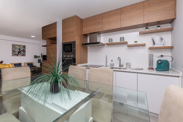 A modern kitchen with wooden cabinets, a glass dining table, and a coffee machine.