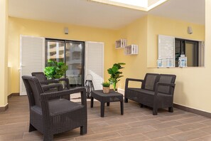 A balcony with wicker furniture, potted plants, and a tiled floor.