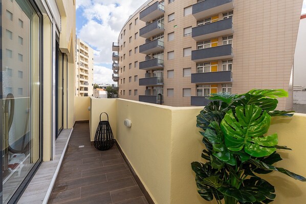 A narrow balcony with a potted plant, a hanging chair, and a view of adjacent buildings.