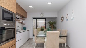 A modern kitchen with built-in appliances, a dining area with a glass table and beige chairs, and a view into the living area. - Ophyris Apartment, Praia da Rocha, WiFi, AC !New! (Portimão)