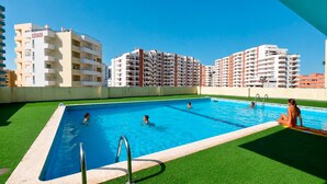 A swimming pool with a green artificial turf border, surrounded by high-rise residential buildings. - Ophyris Apartment, Praia da Rocha, WiFi, AC !New! (Portimão)