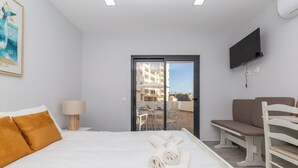 A hotel room with a bed, a chair, a TV, and a balcony with a view of buildings. - Ophyris Apartment, Praia da Rocha, WiFi, AC !New! (Portimão)