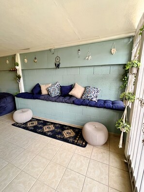 A room with a teal-colored wall, a low bench with cushions, a patterned rug, and two round ottomans.