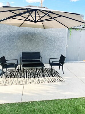An outdoor patio with a table and chairs, a patterned rug, and a large umbrella.