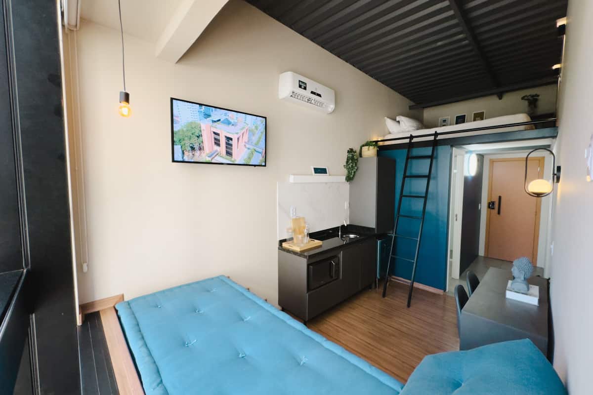 A compact bedroom with a bunk bed, a kitchenette, and a TV on the wall.