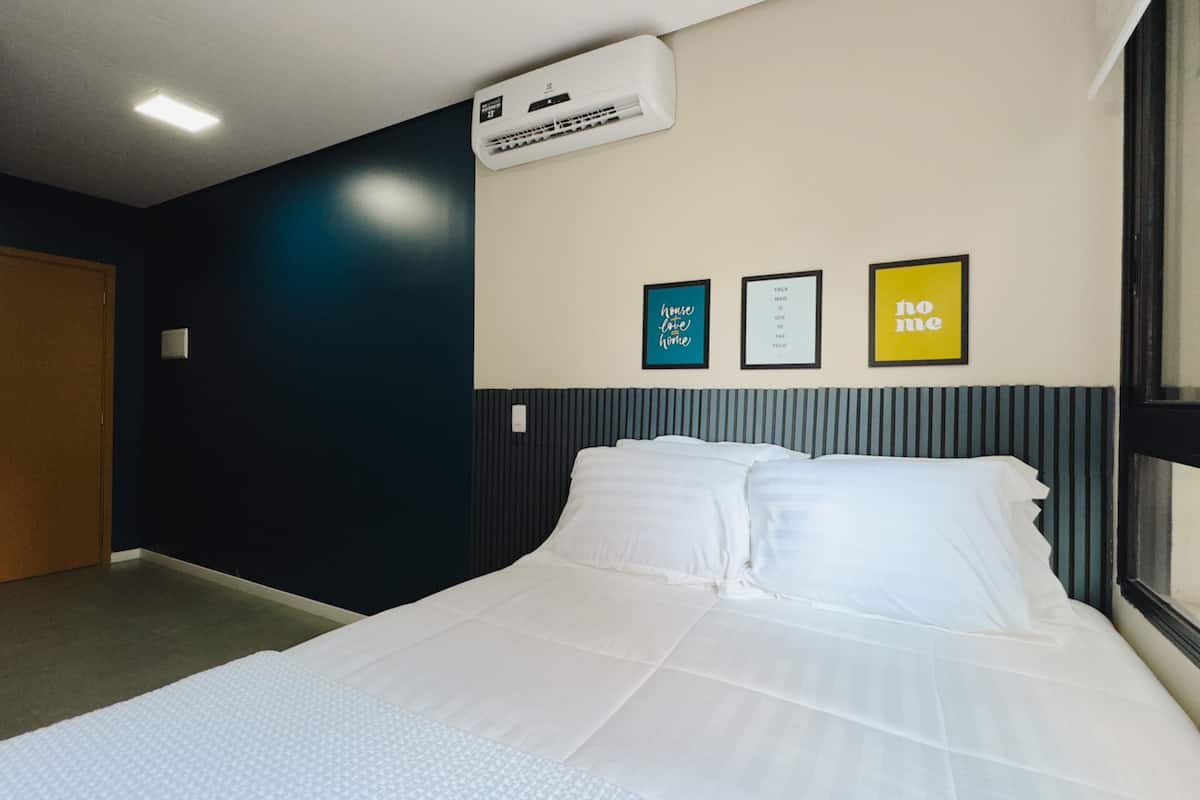 A hotel room with a bed, a wall-mounted air conditioner, and three framed signs on the wall.