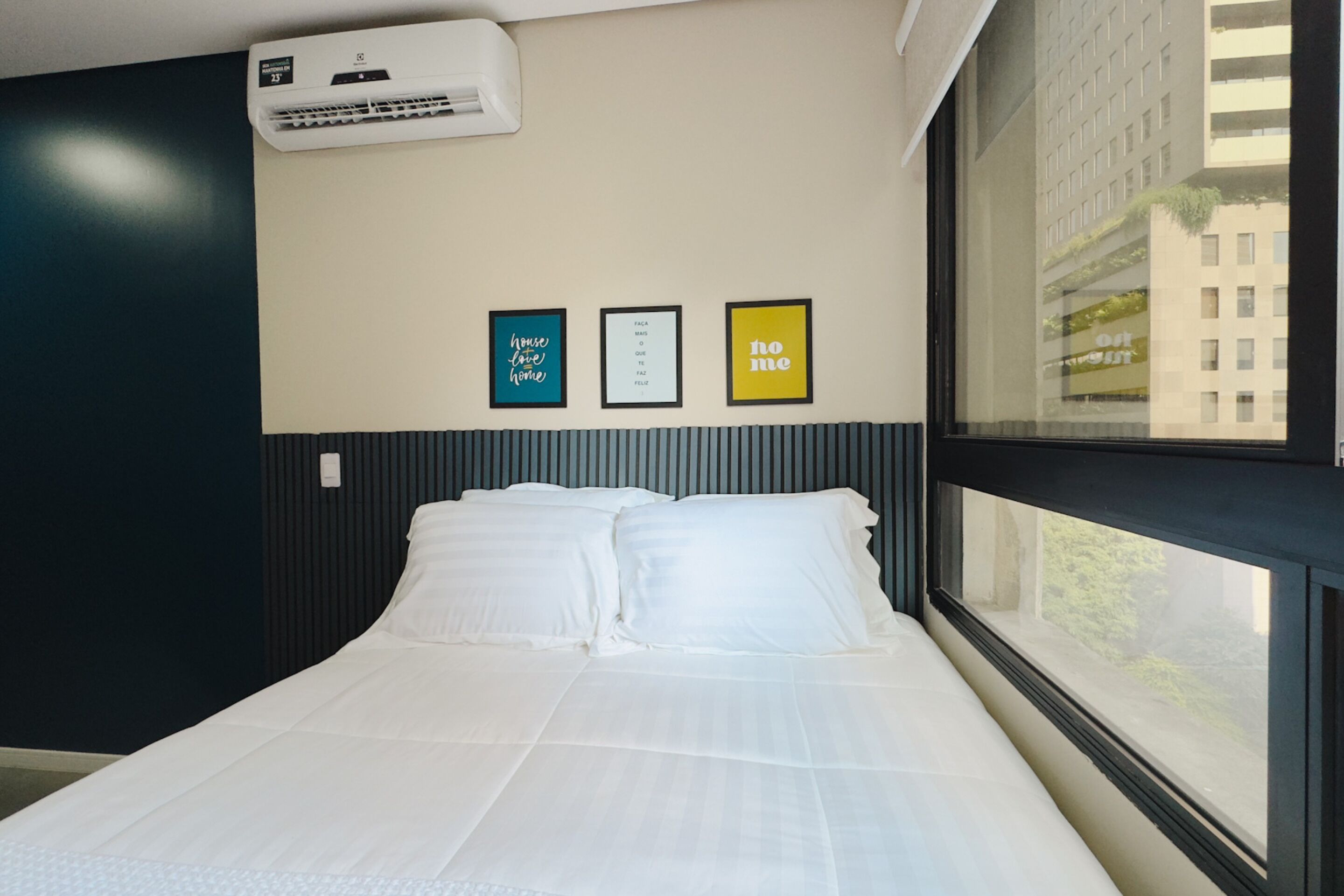 Habitación de hotel con cama, unidad de aire acondicionado y tres cuadros en la pared.