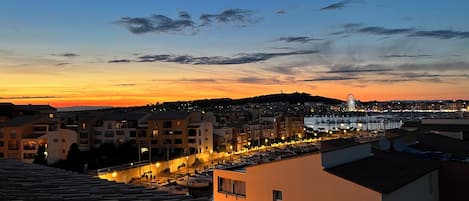 A coastal town at dusk with buildings, a marina, and a Ferris wheel.