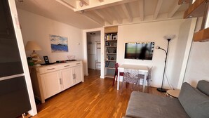 Een woonkamer met een bank, een eettafel met stoelen, een keuken met een kast, en een aan de muur bevestigde televisie.