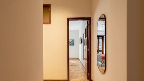 A hallway with a herringbone floor, a door leading to a room with a bed and a red chair, and a mirror on the wall. - Prized Spacious Flat | Balcony by HostWise (Porto)