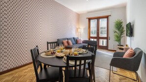A dining area with a round table set for breakfast, a sofa, and a TV mounted on the wall. - Prized Spacious Flat | Balcony by HostWise (Porto)