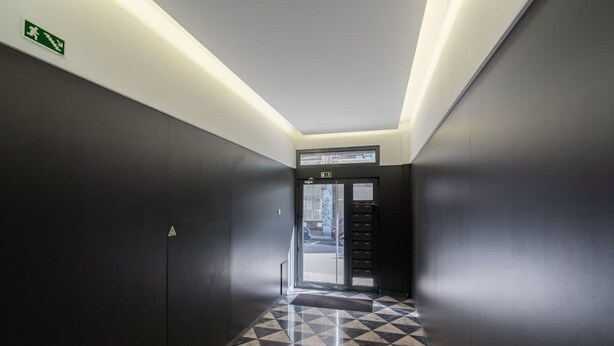 A hallway with a checkered floor, a door with a sign above it, and a wall-mounted emergency exit sign. - Prized Spacious Flat | Balcony by HostWise (Porto)