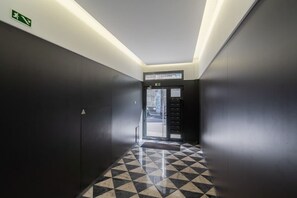 A hallway with a checkered floor, a door with a sign above it, and a wall-mounted emergency exit sign.