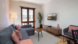 A modern living room with a grey sofa, a small wooden coffee table, and a TV mounted on the wall. - Prized Spacious Flat | Balcony by HostWise (Porto)