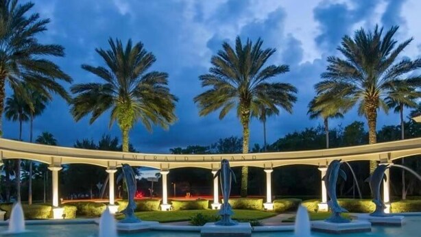 Zona de piscina con palmeras, un paseo techado y una escultura de delfín.