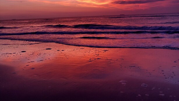 Een strand bij zonsondergang met golven en een roze lucht.