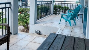Een overdekt buitengebied met een houten bank, twee turquoise stoelen en een betegelde vloer.