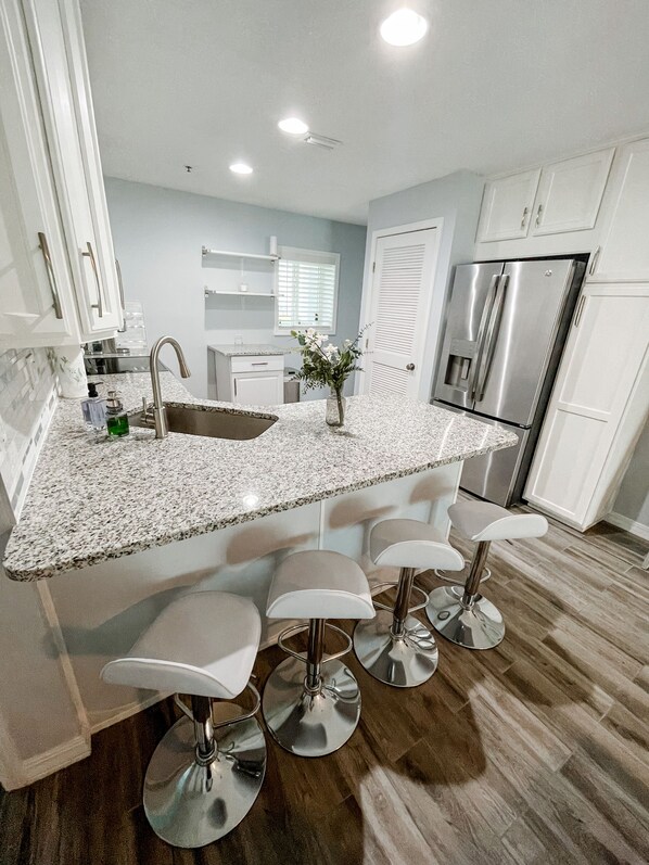 A modern kitchen with a granite countertop, stainless steel appliances, and bar stools.