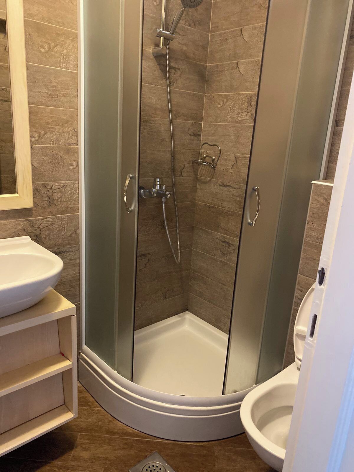 A glass-enclosed shower stall with a white sink and toilet in a corner bathroom.