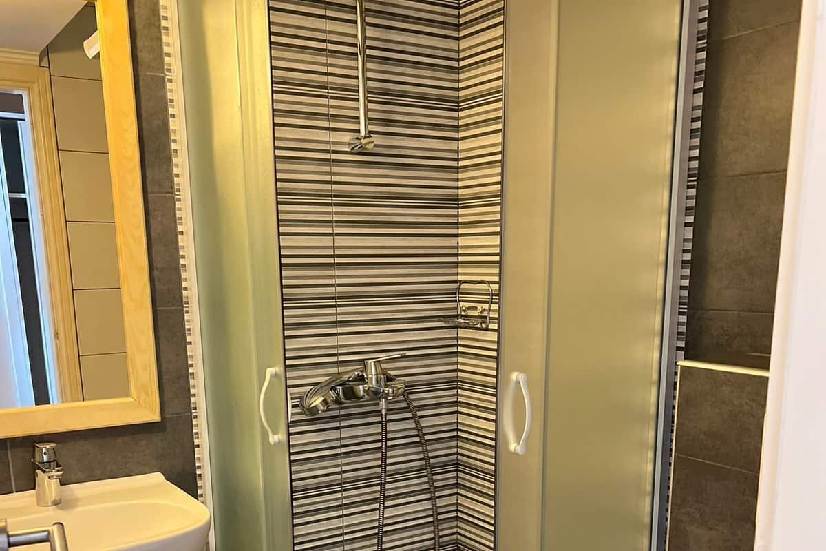 Un baño moderno con ducha de vidrio, lavamanos blanco y retrete.