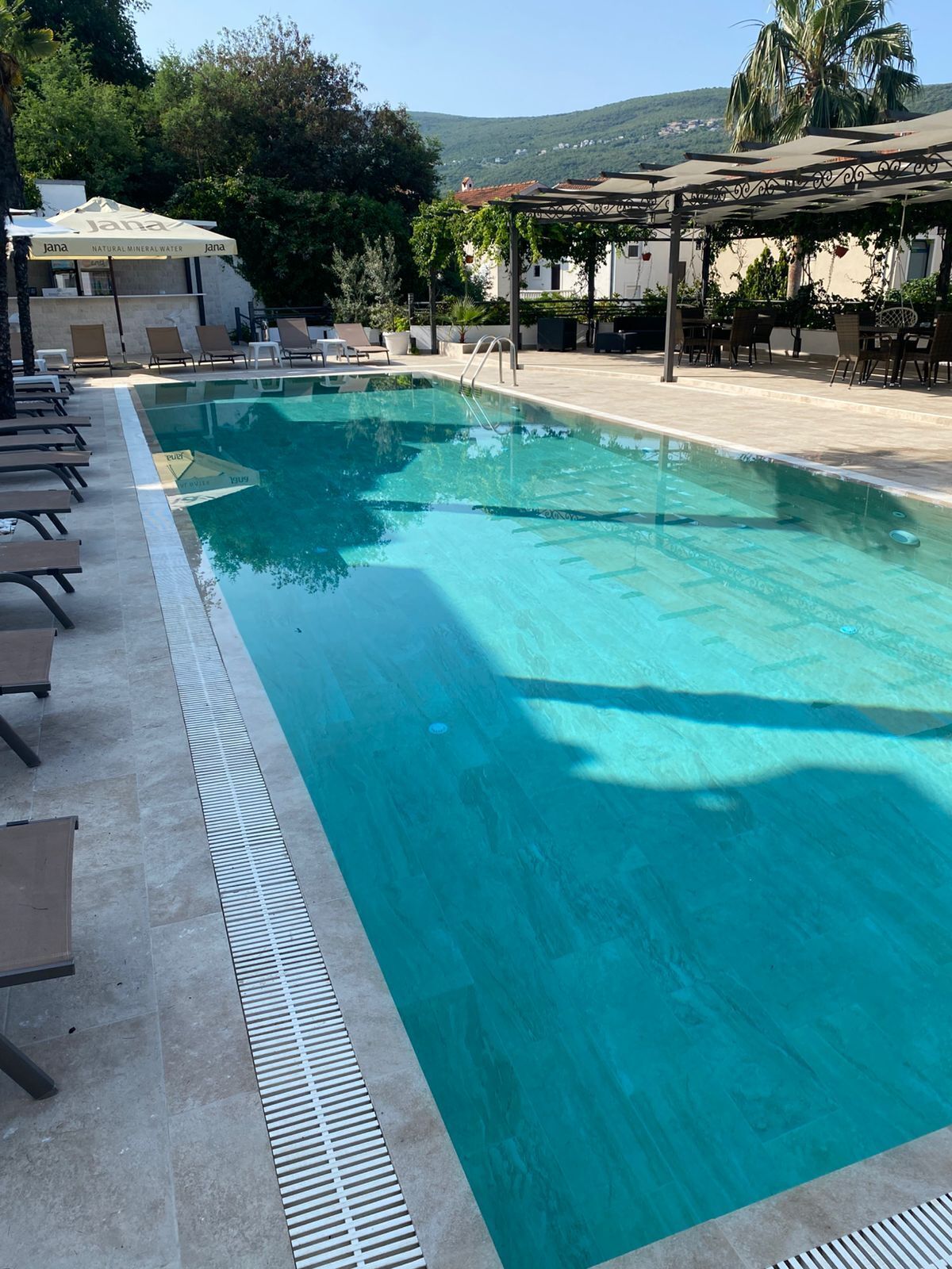 A rectangular swimming pool with clear blue water, surrounded by lounge chairs and a pergola.