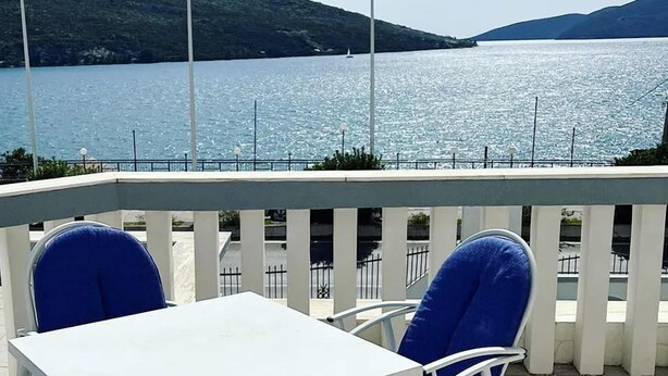 A terrace with a white table and blue chairs, overlooking a calm lake with hills in the background. - XANADU (Kumbor)