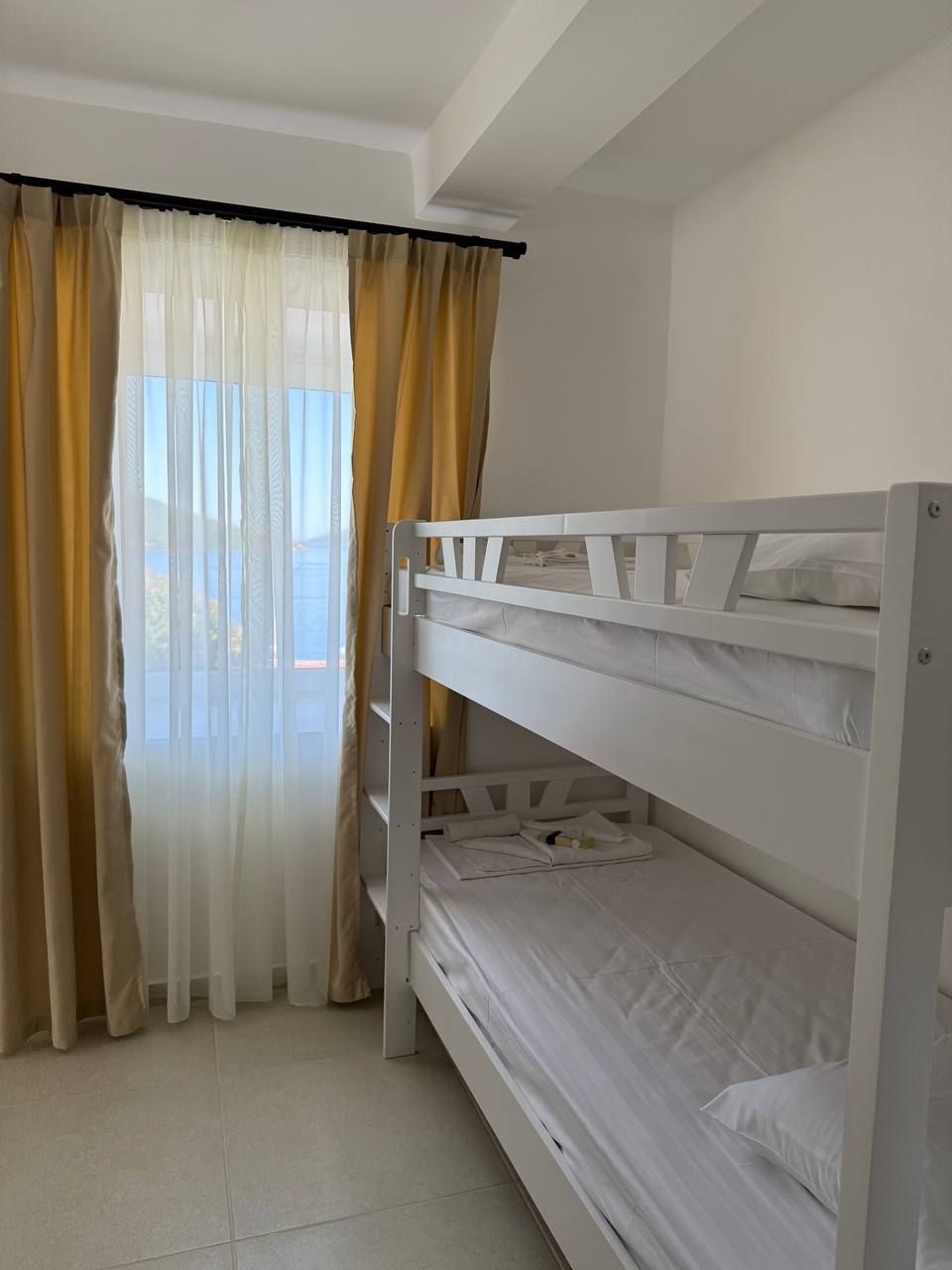 A bunk bed room with a view of the sea through sheer curtains.