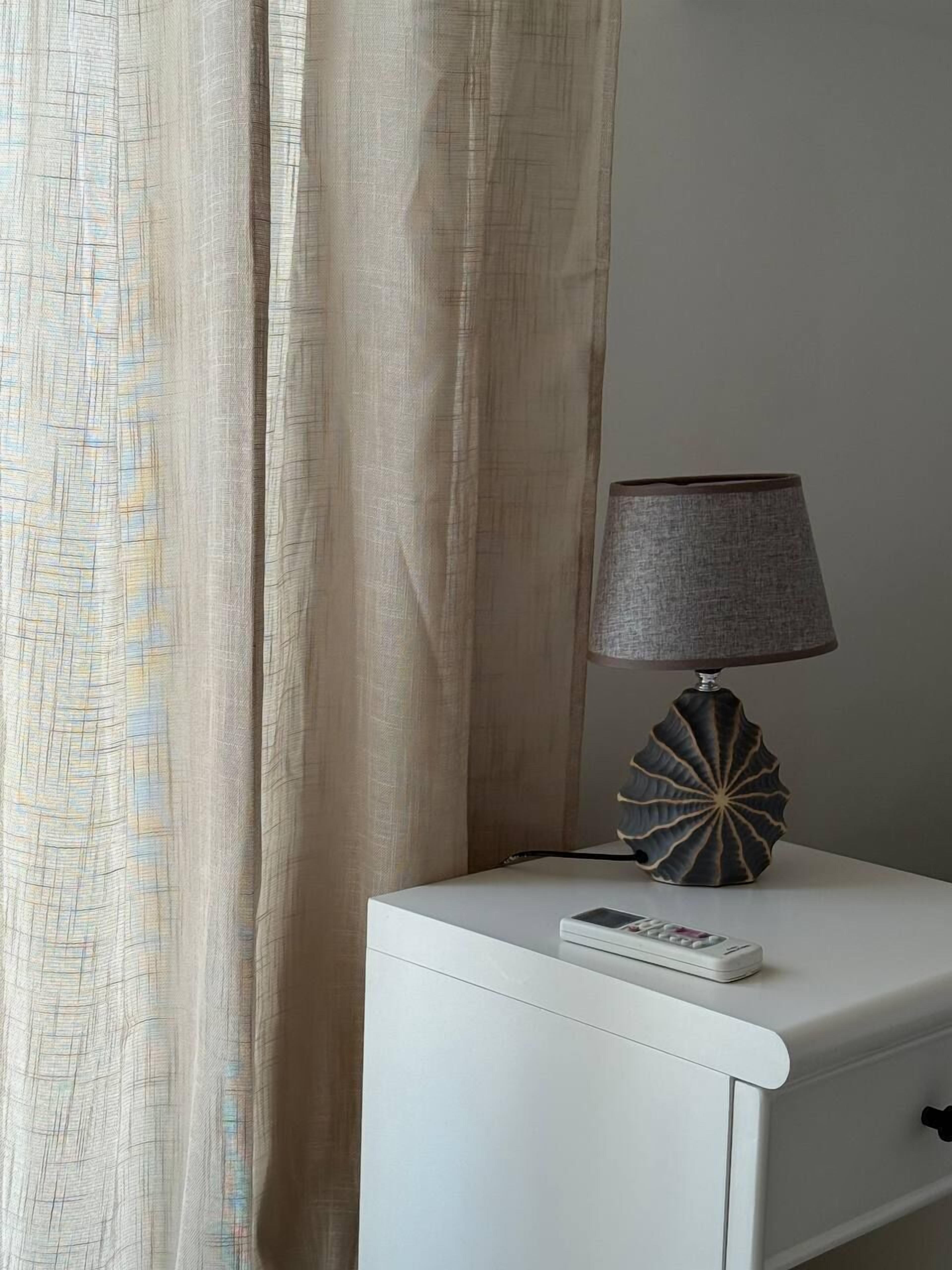 Een wit nachtkastje met een lamp en een afstandsbediening.