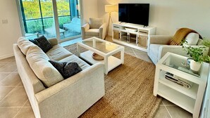 Ein modernes Wohnzimmer mit Sofa, Couchtisch, Fernseher und Blick auf einen Balkon.
