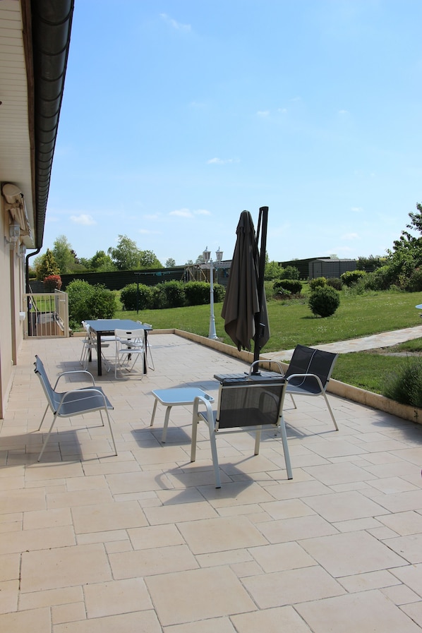 An outdoor patio with a table and chairs, an umbrella, and a view of a well-maintained garden.