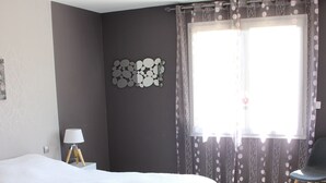 Un dormitorio con cama, una silla, una lámpara y una ventana con cortinas.