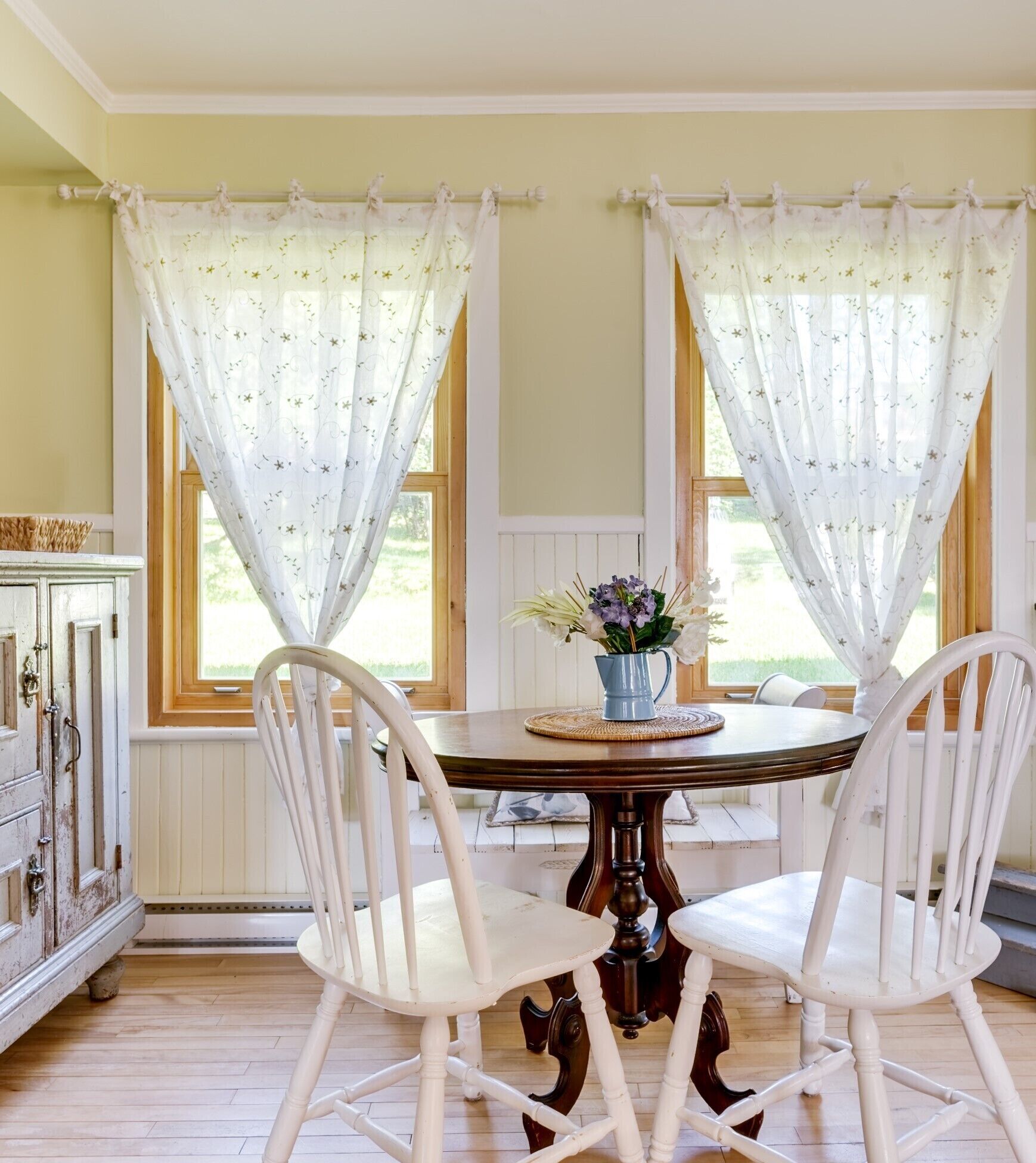 A dining area with a round table, two white chairs, and a vase with flowers.