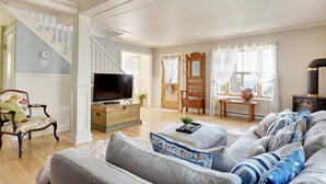 A living room with a sofa, a television, a wooden chest, a chair, and a staircase. - Ancestral home, Charlevoix - Saint-Irénée Beach & St. Lawrence River view (Saint-Irénée)