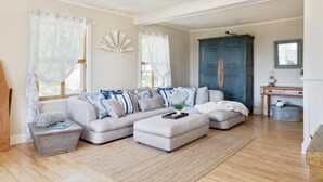 A cozy living room with a sectional sofa, a small side table, and a blue cabinet. - Ancestral home, Charlevoix - Saint-Irénée Beach & St. Lawrence River view (Saint-Irénée)