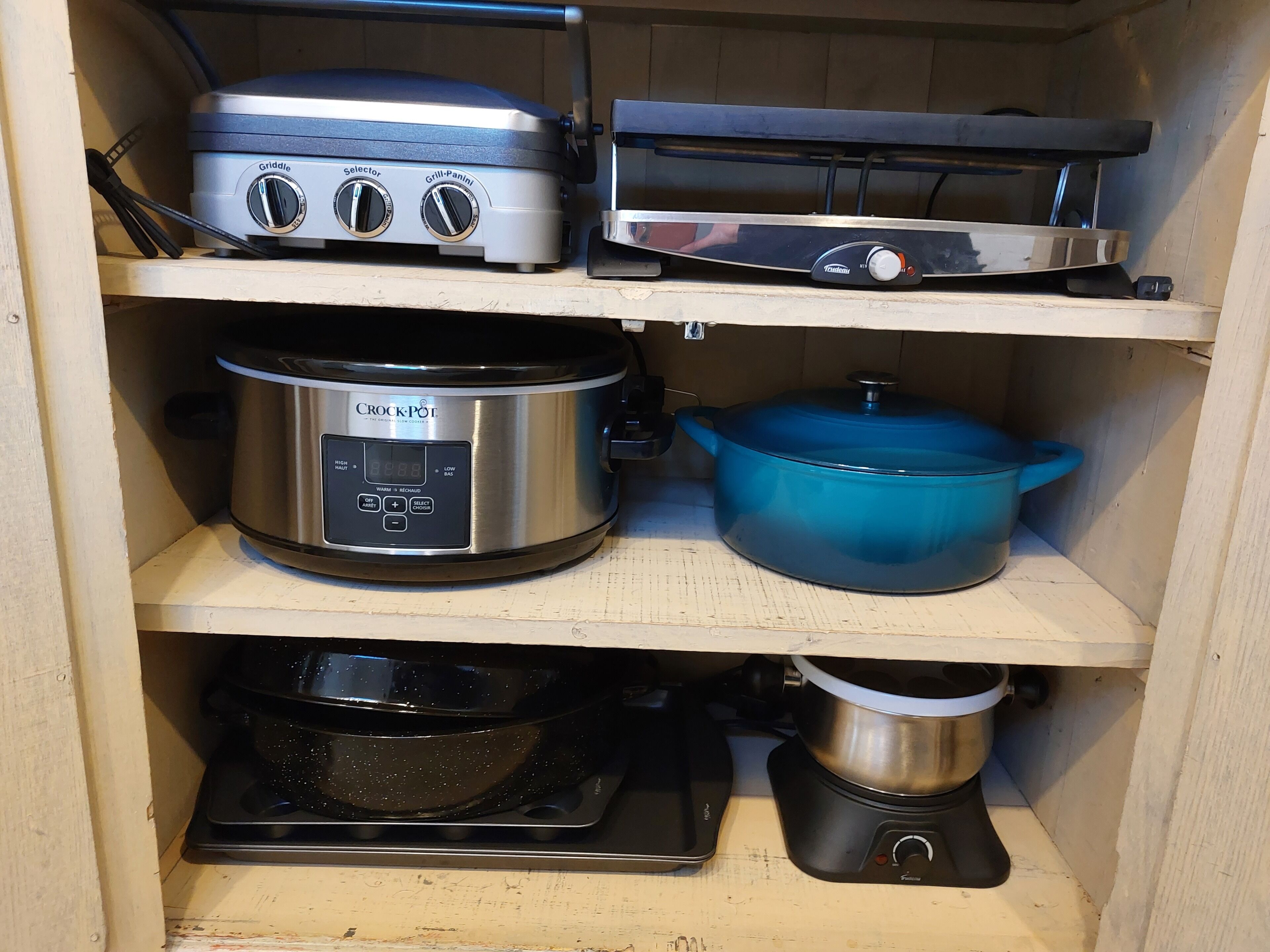 A kitchen with a griddle, a slow cooker, a pressure cooker, and a blue pot on the shelves.