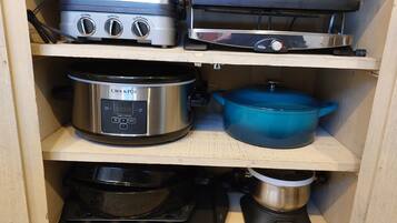 A kitchen with a griddle, a slow cooker, a pressure cooker, and a blue pot on the shelves.